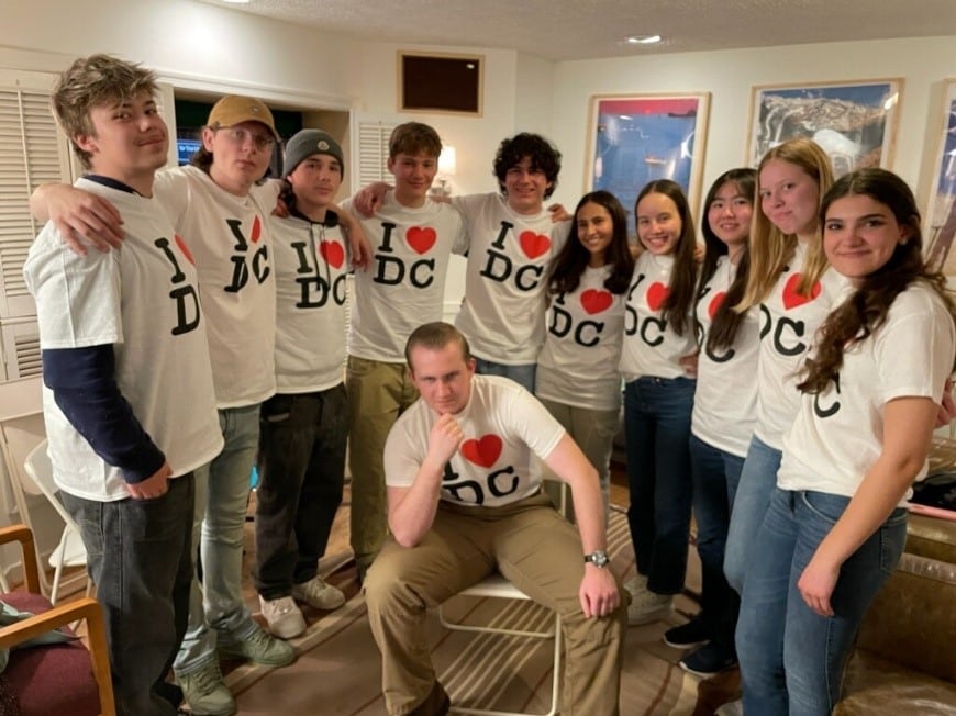 10 students pose standing in a semi circle with another student kneeling in the middle. All are wearing white I heart DC shirts.